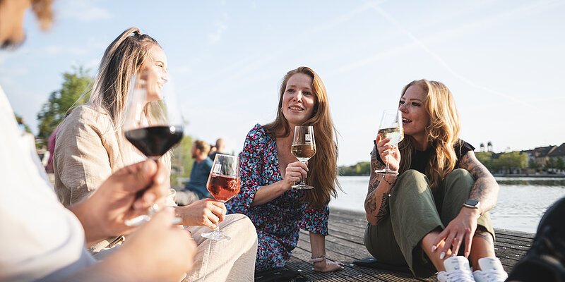 Kitzinger Stadtschoppen Eine Personengruppe sitzt am Kitzinger Main und trinkt ein Glas Wein.