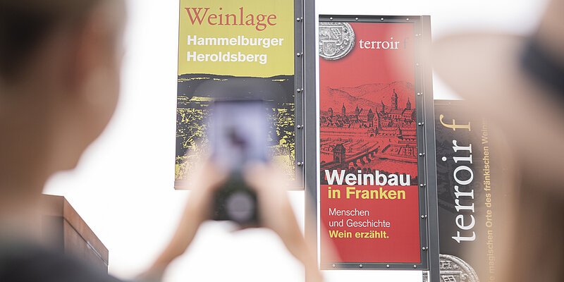 Fahnen des Terroir f in Hammelburg werden fotografiert Eine Frau fotografiert mit ihrem Smartphone die drei Fahnen des Terroir f in Hammelburg